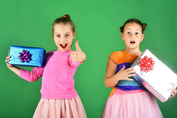 Enfants avec des visages excités posent avec des cadeaux sur fond vert . — Photo