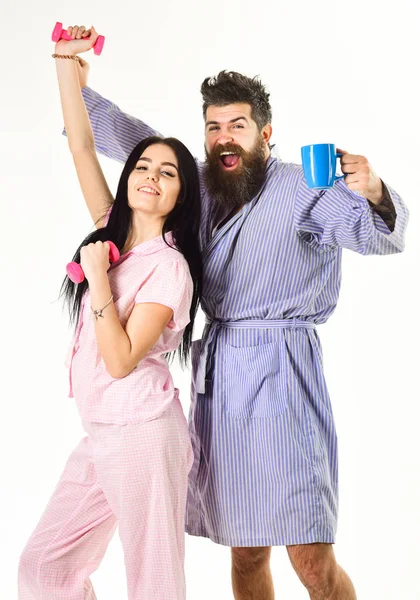 Pareja, familia con caras soñolientas, llena de energía. Pareja enamorada en pijama, albornoz aislado sobre fondo blanco. Concepto de rutina matutina. Chica con mancuerna, hombre con taza de café — Foto de Stock