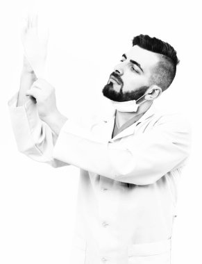 Sakallı bir cerrah ciddi bir yüzle eldiven takıyor.