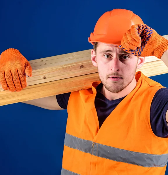 木工概念。木匠, 木工, 工人, 建设者在肩膀上运载木横梁。男子戴着防护手套, 戴着头盔的遮阳帽, 在头部、蓝色的背景上矫正安全帽, 合上 — 图库照片