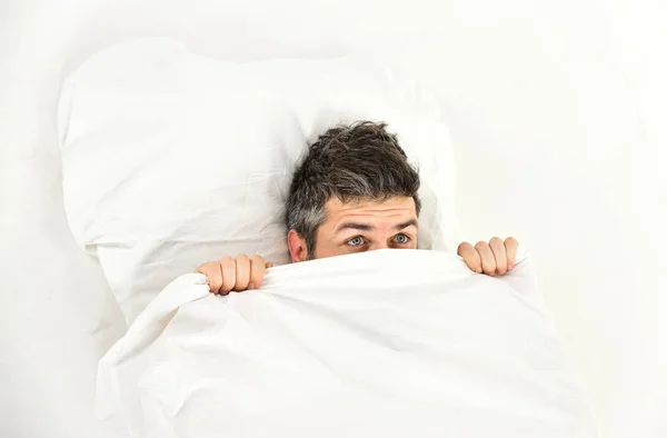 Sleepyhead concept. Guy hides face under blanket.