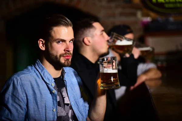 Friends drink beer together on blurred pub background.