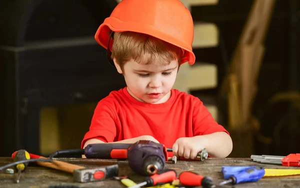 Toddler on busy face plays with bolts at home in workshop. Kid boy play as handyman. Child in hard hat, helmet playing with hex bolts as builder or repairer, handcrafting. Handcrafting concept — Stock Photo, Image