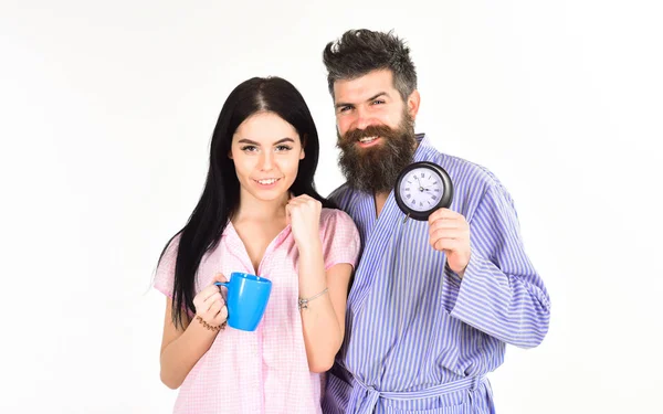 Man and girl in pajamas get up on time, white background. Perfect morning with coffee. Couple in love drink morning coffee or tea. Family of man and woman with cup and alarm clock
