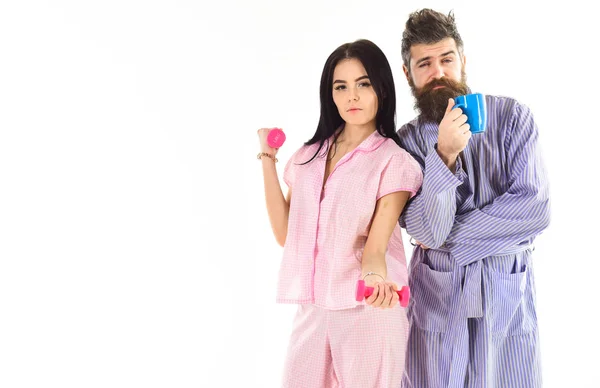 Fille avec haltère, homme avec tasse de café, isolé sur fond blanc. Couple amoureux en pyjama, peignoir dos à dos. Couple, famille au visage endormi dans la routine matinale. Concept d'énergie du matin — Photo