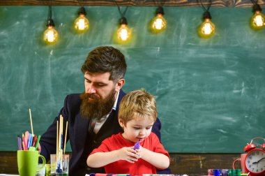 Çocuk ve öğretmen meşgul yüzleri boyuyor, resim çiziyor. Sakallı öğretmen, baba ve küçük oğlu sınıfta resim çizerken, yaratırken, arka planda karatahta çizerken. Yetenek ve yaratıcılık kavramı
