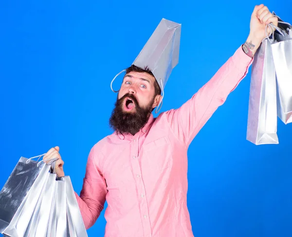 Typen, die in der Verkaufssaison mit Rabatten einkaufen. Mann mit Bart und Schnurrbart trägt Einkaufstaschen, blauer Hintergrund. Hipster mit glücklichem Gesicht und Tasche auf dem Kopf sind süchtig nach Shopaholic. Einkaufskonzept — Stockfoto