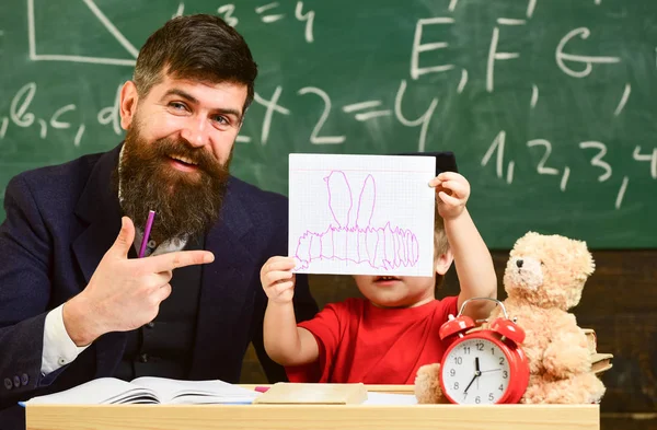 Lärare och elev i mortarboard, svarta tavlan på bakgrund. Far med skägg, lärare lär son, kid boy. Kid studier med lärare, nära häfte, klocka, leksak. Undervisning barn koncept — Stockfoto