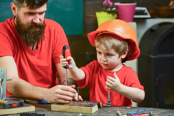 Apja, szülő szakáll tanítás kis fia eszköz csavarhúzóval. Fiú, gyermek elfoglalt védő sisak, a tanulás csavarhúzóval, apa. Javítási és workshop koncepció — Stock Fotó