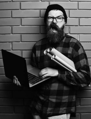 Kaba sakallı, beyaz tenli hippi elinde dizüstü bilgisayar ve el işi kâğıdı tutuyor.