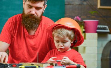 Erkeksi görevleri kavramı. Çocuk, Çocuk koruyucu kask hobnails baba ile çekiç için öğrenme içinde meşgul. Baba, sakallı hobnails ve çekiç kullanmak için küçük oğlu öğretim üst