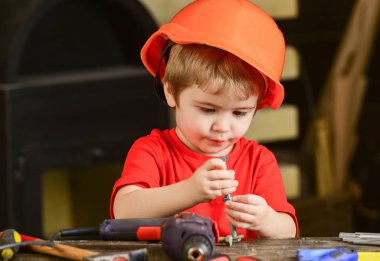 Baret, Oluşturucusu'nu veya repairer, handcrafting onaltılık cıvata ile oynarken kask çocuk. Yürümeye başlayan çocuk meşgul yüzündeki evde atölyede civata ile oynuyor. Kavram handcrafting. Çocuk Çocuk tamirci oynamak.