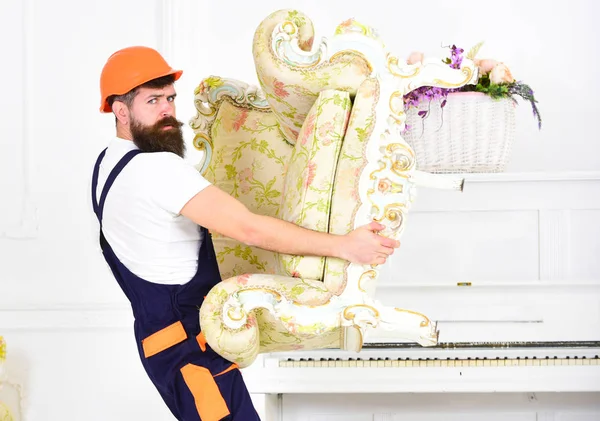 Fuerte barbudo llevando un viejo sillón solo. Mover en casco naranja aislado sobre fondo blanco — Foto de Stock