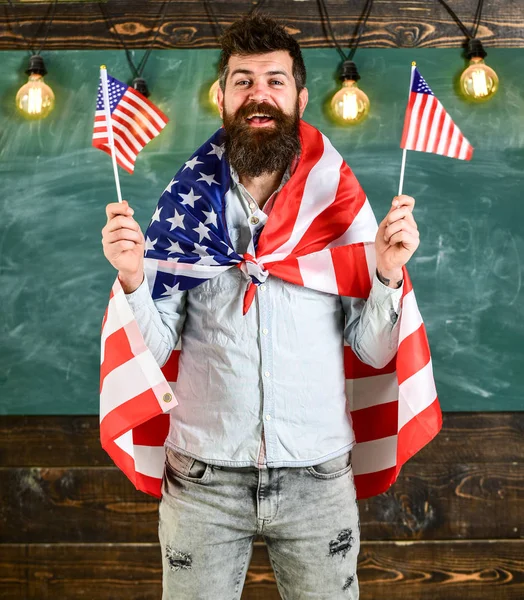 Profesora americana ondea con banderas americanas. Programa de intercambio de estudiantes. Concepto de educación patriótica. Hombre con barba y bigote en la cara feliz sostiene banderas de EE.UU., en el aula, pizarra en el fondo — Foto de Stock