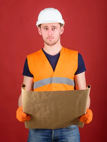 Engineer, architect, labourer, builder on strict face holds old blueprint in hands. Man, handyman in helmet, hard hat holds building plan, red background. Engineering concept — Stock Photo, Image