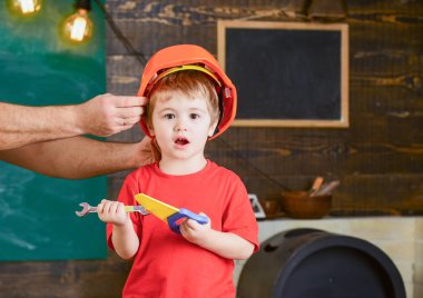 Oyuncak araçları ile oynayan heyecanlı çocuk. Sarışın çocuk atölyede bağırarak. Baba küçük yardımcısı. Turuncu koruyucu kask tutan erkek el