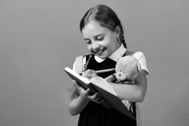 Kız mavi not defterinde yazıyor ve oyuncak ayı tutar