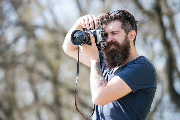 Young male photographer taking pictures in the park with vintage camera, hobby and leisure activity concept. Bearded hipster searching for best spot for photo shooting — Stock Photo, Image