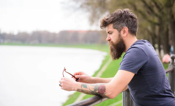 Homem com barba e bigode com óculos de sol, ribeirinha no fundo. Hipster na cara pensativa em pé à beira do rio, pensando, sonhando, desfocado. Conceito de reflexão e pensamentos — Fotografia de Stock