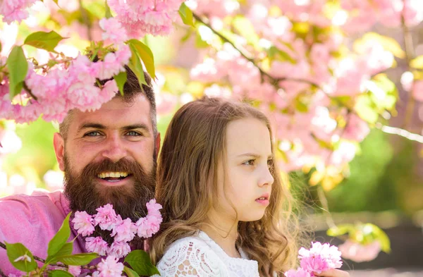 Fatherhood concept. Girl with dad near sakura flowers on spring day. Child and man with tender pink flowers in beard. Father and daughter on happy and calm faces , sakura background — Stock Photo, Image