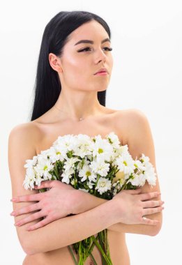 Sağlıklı ciltle pürüzsüz kadınla çekici görünüyor. Bayan göğüsler üzerinde beyaz izole çiçekli kapsar. Sakin yüz çıplak kız papatya çiçeği göğüsler önünde tutar. Doğal kozmetik kavramı