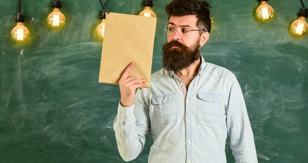 Magabiztos tanár vagy üzletember állandó előtt Palatábla könyvet tart a kezében. A szemüvegek tudós tartja könyv, háttér, másol hely chalkboard — Stock Fotó