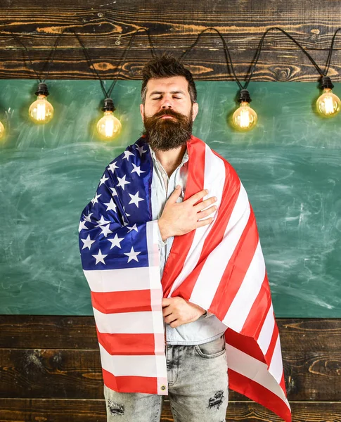 Koncepcja edukacji patriotycznej. Amerykański nauczyciel objęte z amerykańską flagą. Nauczyciel uczy kochać ojczyznę, Stany Zjednoczone Ameryki. Człowiek z broda i wąsy na poważne twarz z flaga Usa, tablica na tle — Zdjęcie stockowe