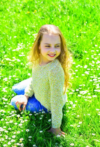 Kız grassplot, arka planı yeşil çimlere oturur. Altın Çağ kavramı. Yüz gülümseyerek kıza harcamak açık havada eğlence. Çocuk çayır otururken bahar güneşli hava keyfini çıkarın