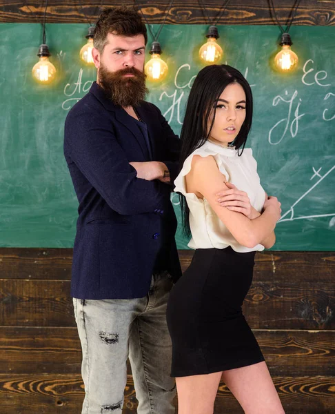 Мужчина с бородой и сексуальная учительница стоят в классе, доска на заднем плане. Концепция партнеров. Леди и хипстер работают вместе в школе. Учитель и строгий школьный учитель выглядят уверенно — стоковое фото