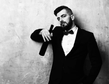 Süitte şık sakallı bir adam bir şişe şarap tutuyor.