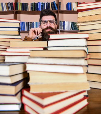 Öğretmen ya da öğrenci sakallı gözlük takmaz, defocused kitaplar ile masada oturur. Bilimsel araştırma kavramı. Adam arasında kazık kitap kütüphane, kitap rafı arka plan üzerinde düşünceli yüzünde
