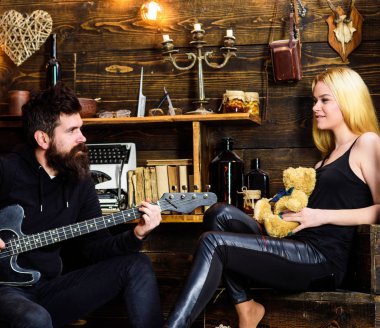 Romantik tarih kavramı. Çift Romantik akşam, ahşap iç arka plan geçirmek. Rahat yüzleri aşık çift romantik atmosferinin keyfini çıkarın. Man oyun gitar iken Bayan oyuncak ayı elinde tutar.