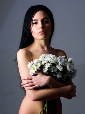 Sağlıklı ciltle pürüzsüz kadınla çekici görünüyor. Doğal kozmetik kavramı. Sakin yüz çıplak kız papatya çiçeği göğüsler önünde tutar. Bayan göğüsler çiçeklerle, gri arka plan kapsar.