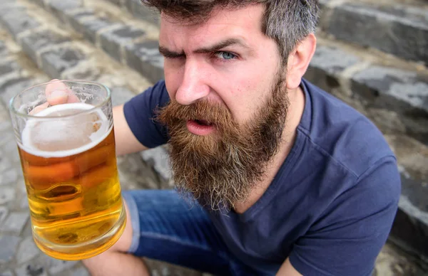 Man met baard en snor houdt glas met bier tijdens zit op stenen trappen, intreepupil. Guy verhogen van glas met bier van het vat. Hipster op strikte gezicht dranken bier buiten. Viering concept — Stockfoto