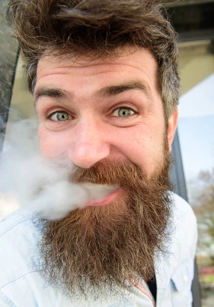 Verdunstungskonzept. Hipster mit zerzausten Haaren und grau auf entspannt fröhlichem Gesicht, aus dem weißer Rauch steigt. Mann mit Raucherbart und Schnurrbart, Bauhintergrund — Stockfoto