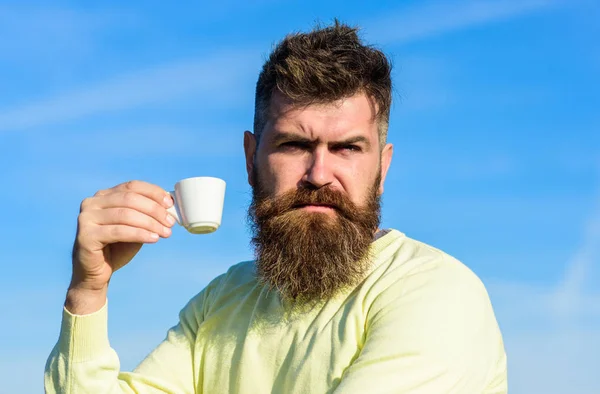 Skäggig man med espresso mugg, drycker kaffe. Mannen med skägg och mustasch på strikt ansikte drycker kaffe, blå himmel bakgrund, oskärpa. Kaffe gourmet koncept. Man med långt skägg njuta av kaffe — Stockfoto