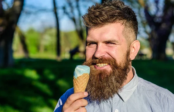 Man with long beard enjoy ice cream, close up. Chilling concept. Man with beard and mustache on happy face eats ice cream, nature background, defocused. Bearded man with ice cream cone