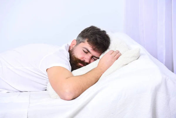 Homem de camisa deitado na cama, parede branca no fundo. Um tipo calmo a dormir em lençóis brancos e almofadas. Macho com barba e bigode dormindo, relaxando, dormindo, descansando. Conceito de sesta e sesta — Fotografia de Stock