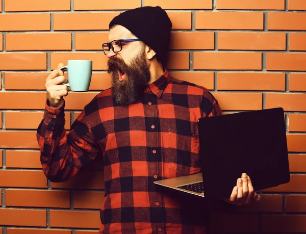 Brutalny, biały hipster trzymający laptopa z kubkiem — Zdjęcie stockowe