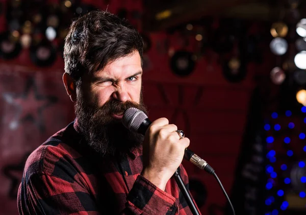 Músico com barba e bigode cantando no karaoke. Conceito de estrela de rock. Homem com rosto entusiasta detém microfone, canto canção, karaoke fundo clube. O tipo gosta de cantar de forma agressiva — Fotografia de Stock