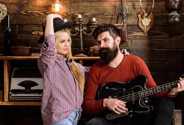 Romantic evening concept. Lady and man with beard on happy faces hugs and plays guitar. Couple in love spend romantic evening in warm atmosphere. Couple in wooden vintage interior enjoy guitar music