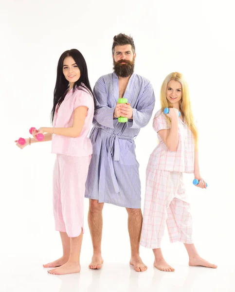 Bearded man with sporty ladies. Fitness morning concept. Company of friends with dumbbells in domestic clothes, isolated on white background. Trainer, macho with attractive girls do morning exercises