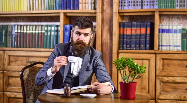 Uomo lettura libroUomo d'affari si siede in interni d'epoca, tiene libro e tazza di tè. Uomo barbuto in completo di lusso nel suo armadietto. Uomo maturo con il viso calmo gode la lettura. Stile di vita di lusso, moda vintage — Foto Stock