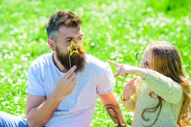 İletişim kavramı. Baba ve kızı, grassplot, arka planı yeşil çimenlerin üzerinde oturur. Aile açık havada eğlence harcamak. Çocuk ve babası eyeglases photo booth özniteliği ile konuşurken poz