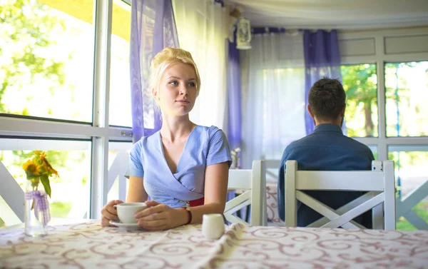 Schöne blonde Mädchen sitzt im Café am Tisch, hält Becher — Stockfoto