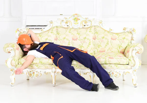 Trabajador barbudo durmiendo en un sofá vintage con casco protector sobre su cara. Constructor cansado disfrutando de un descanso y tomando una siesta en el trabajo — Foto de Stock