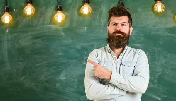 Homem com barba e bigode em pé rosto estrito na frente do quadro. Hipster barbudo em camisa, quadro no espaço de cópia de fundo. Um tipo a apontar com o dedo indicador a bordo. Conceito estrito de professor — Fotografia de Stock