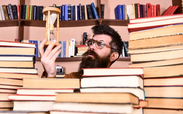 Adam düşünceli yüzünde ise eğitim, kitap rafı arka plan üzerinde kum saati tutar. Dostum, bilim adamı bardaklarda kum saati görünüyor. Zaman akışı kavramı. Öğretmen ya da sakal Kitaplığı'nda eğitim ile öğrenci