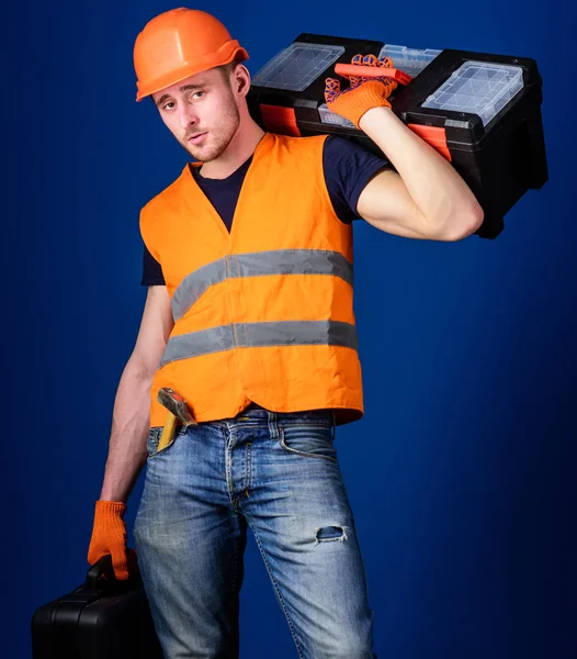 Mannen i hjälm, hård hatt innehar verktygslådan och resväska med verktyg, blå bakgrund. Arbetare, reparatör, reparatör, byggaren på lugna ansikte bär verktygslådan på axeln, redo att arbeta. Reparation servicekoncept — Stockfoto