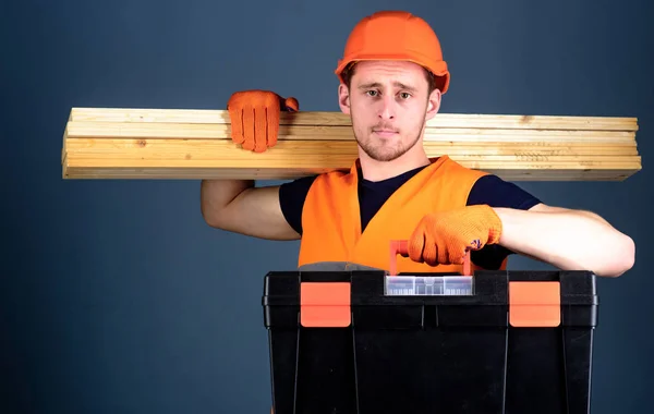 Tischler, Arbeiter, Bauarbeiter, Holzarbeiter mit ruhigem Gesicht trägt Holzbalken auf der Schulter. professionelles Holzarbeiterkonzept. Mann mit Helm, harter Hut hält Werkzeugkiste und Holzbalken, grauer Hintergrund — Stockfoto